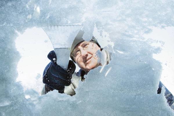 Older man scraping ice off car window