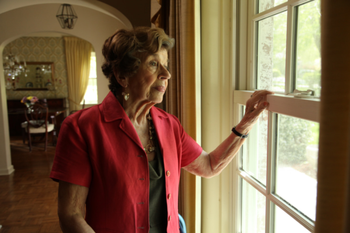 Elderly woman gazes out the window of her home.